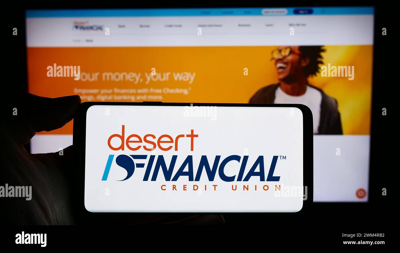 Person holding cellphone with logo of US financial services company Desert Financial Credit Union in front of webpage. Focus on phone display. Stock Photo