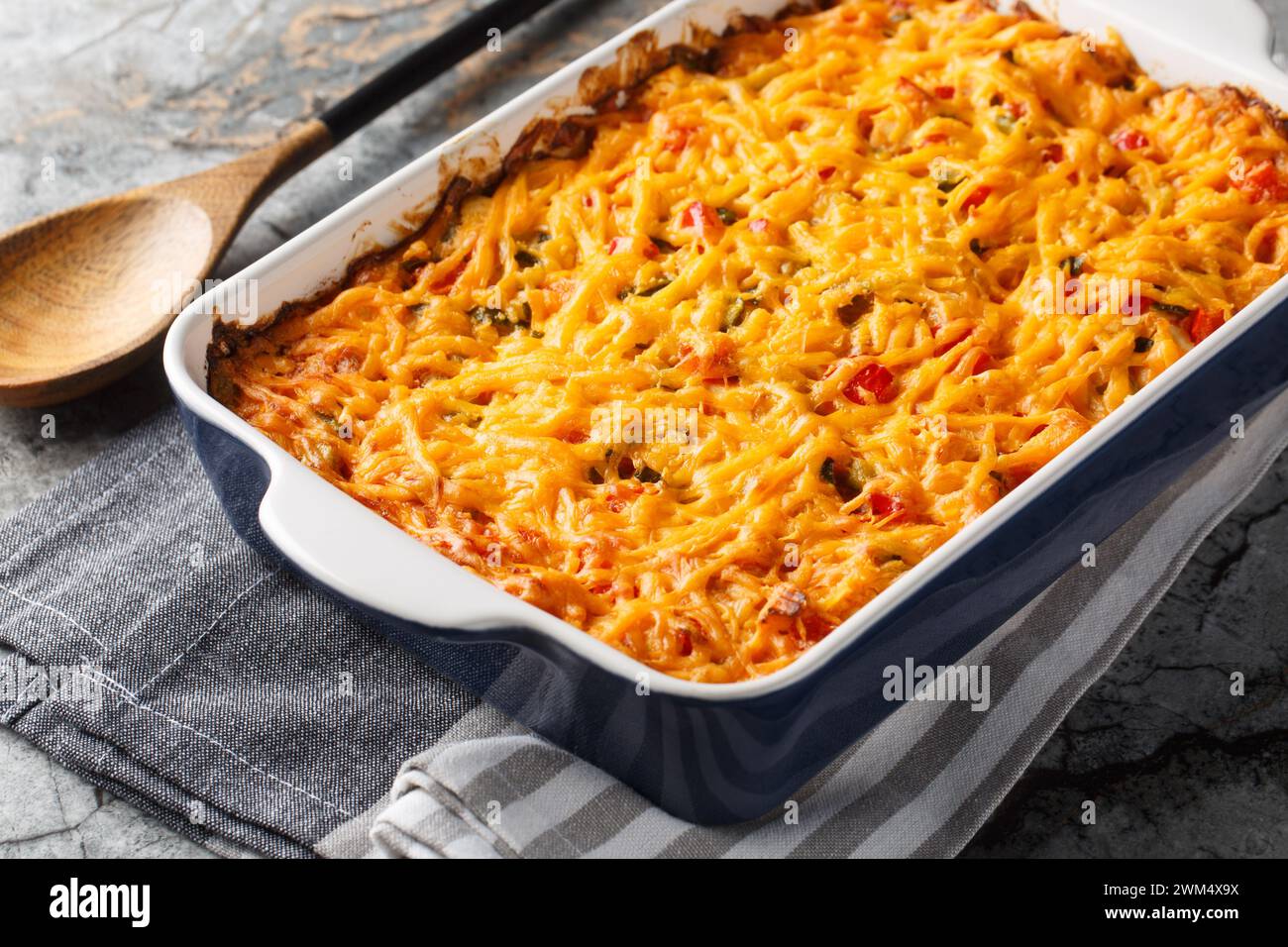 King Ranch Casserole is lined with corn tortillas, then layered with sauce and topped with cheese close-up in a baking dish on a marble table. Horizon Stock Photo