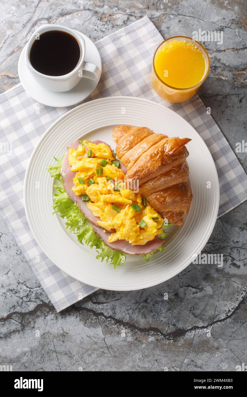 Scrambled eggs ham croissant served with orange juice and coffee close-up on a marble table. Vertical top view from above Stock Photo
