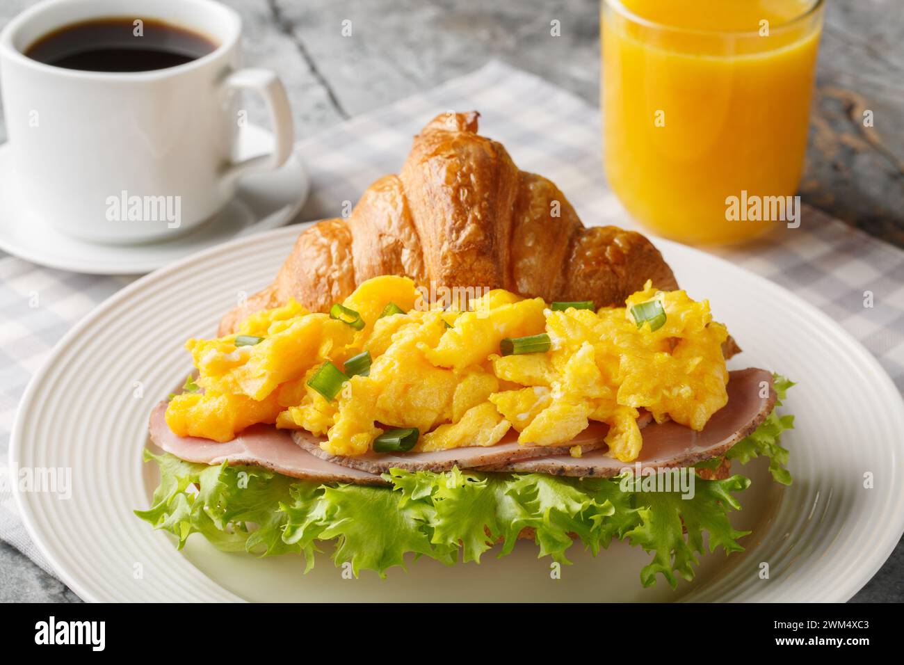 Breakfast Croissant Sandwich with Scrambled Eggs and Ham Served with Orange Juice and Coffee Close-up on a Marble Table. Horizontal Stock Photo
