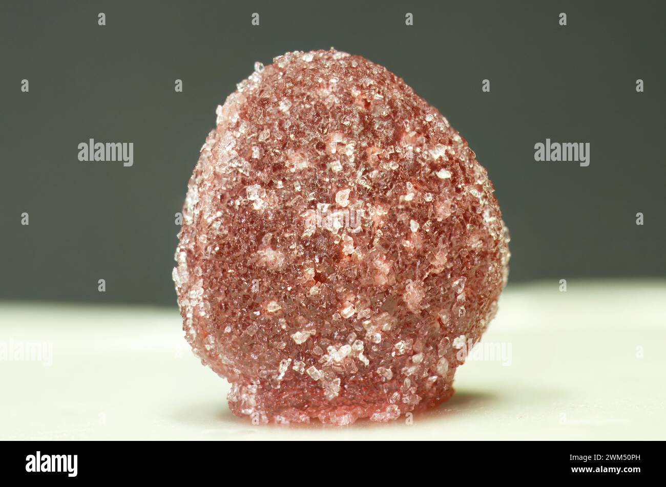 Sugar crystals sprinkled on red gumdrop jelly soft candy in selective focus isolated on dark green background Stock Photo