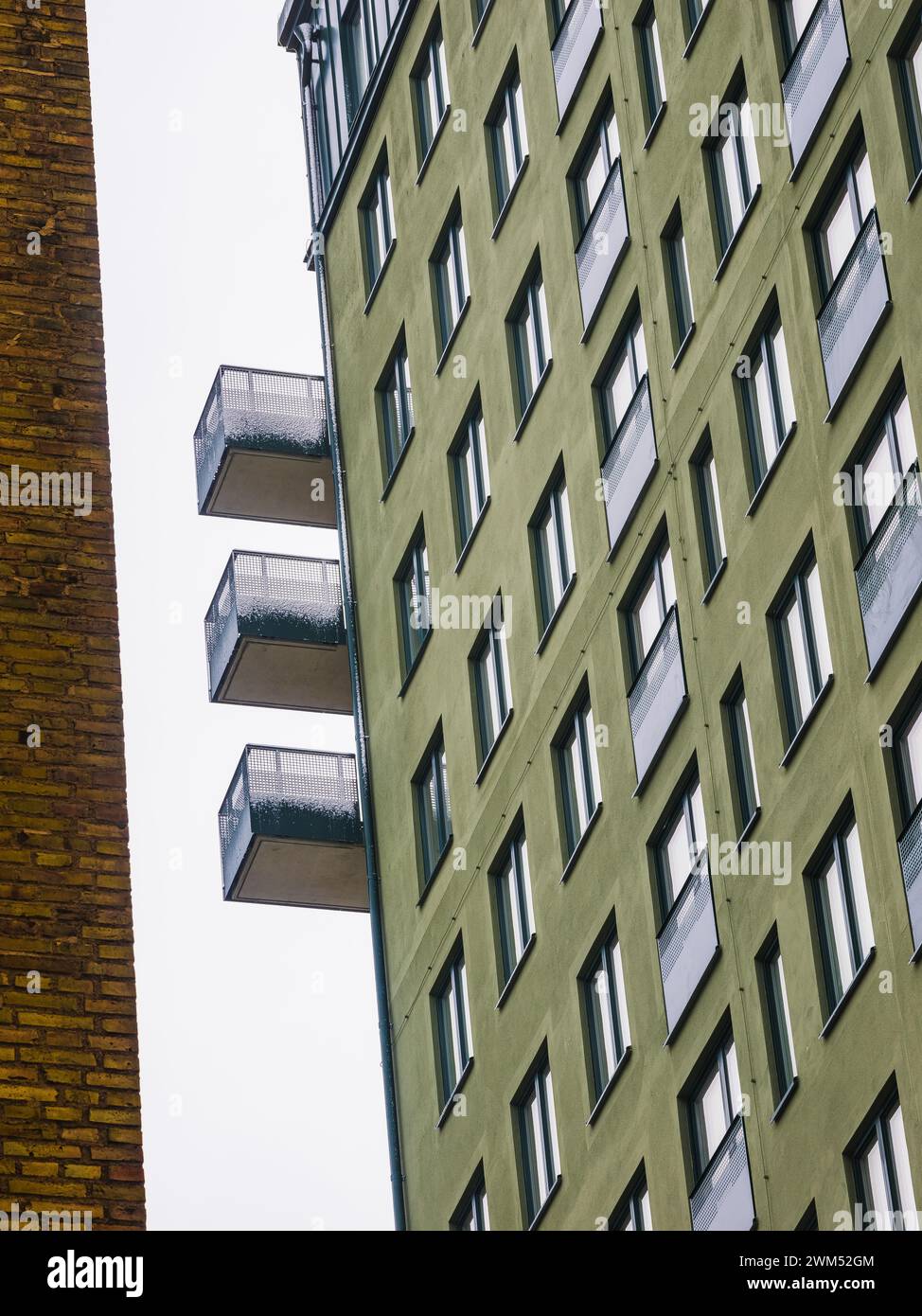 The facade of a contemporary building in Gothenburg is shown, featuring a sequence of balconies protruding against a gray sky. The buildings green ext Stock Photo