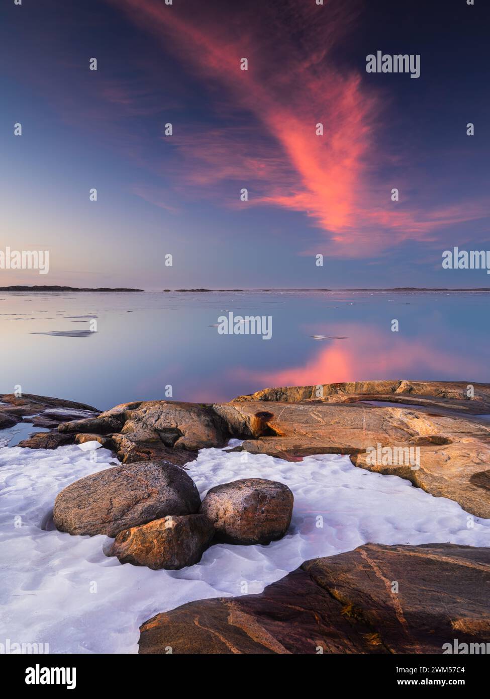 A serene view of Sillvik at sunset with a vibrant display of pink and blue hues in the sky, reflecting upon the tranquil waters. Snow nestles among th Stock Photo