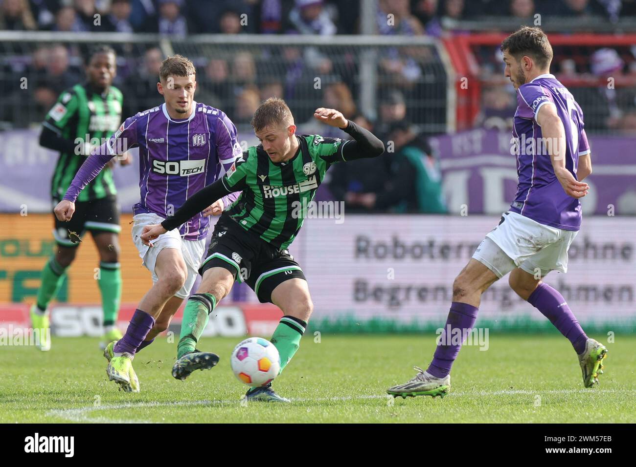 24 February 2024, Lower Saxony, Osnabrück: Soccer: Bundesliga 2, VfL Osnabrück - Hannover 96, matchday 23 at the Stadion an der Bremer Brücke. Osnabrück's Michael Cuisance (l) and Bashkim Ajdini (r) battle for the ball with Hannover's Sebastian Ernst (M). Photo: Friso Gentsch/dpa - IMPORTANT NOTE: In accordance with the regulations of the DFL German Football League and the DFB German Football Association, it is prohibited to utilize or have utilized photographs taken in the stadium and/or of the match in the form of sequential images and/or video-like photo series. Stock Photo