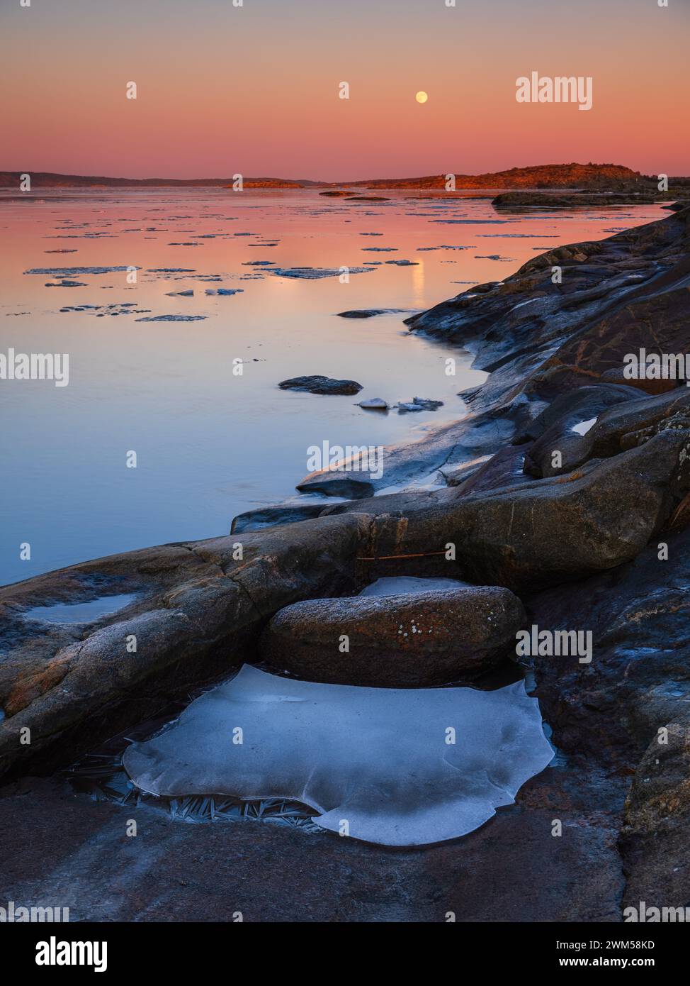 Frozen rocks are scattered across the beach as the sun sets in Sillvik, Sweden. The icy formations add a unique and stark element to the coastal lands Stock Photo
