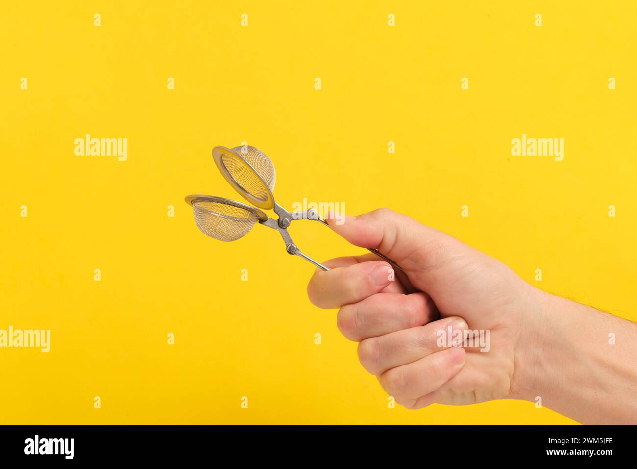 Tea strainer in hand yellow background Stock Photo