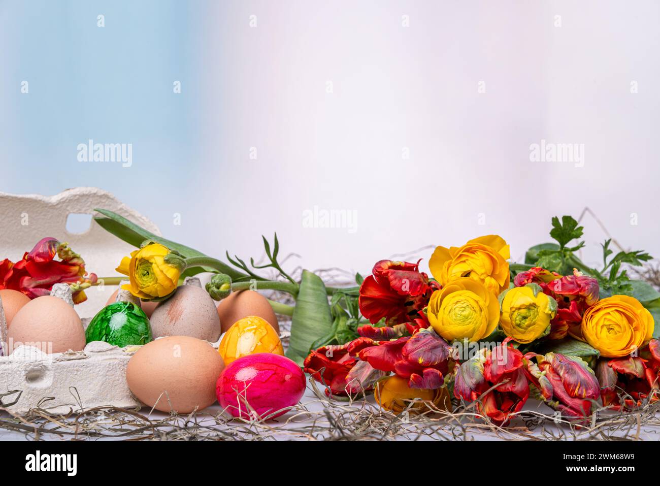 Bunte Ostereier auf einem Tisch mit Bumenstrauß als Postkartenmotiv zu Ostern Stock Photo