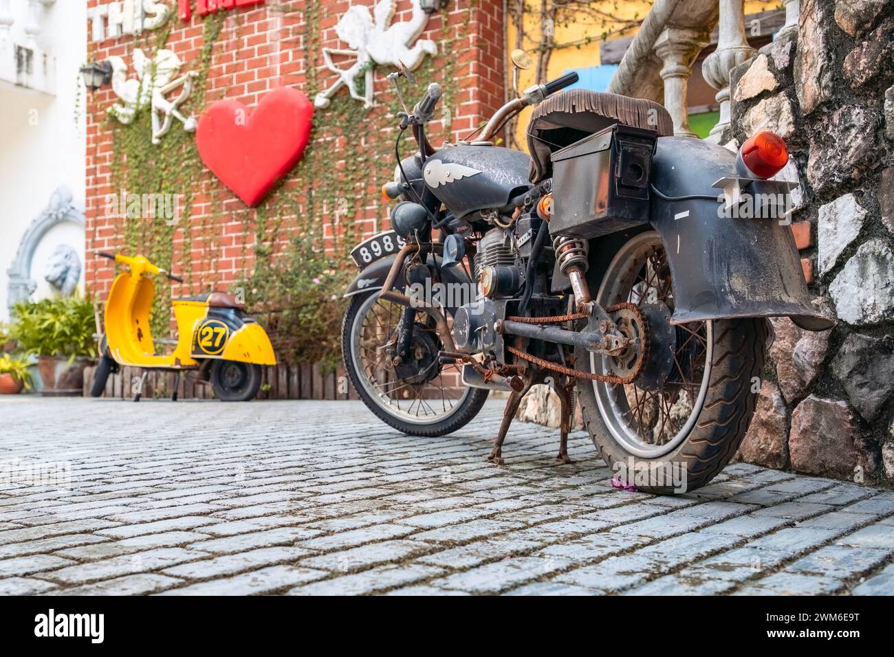 A motorcycle parked by a brick wall with a yellow scooter nearby Stock