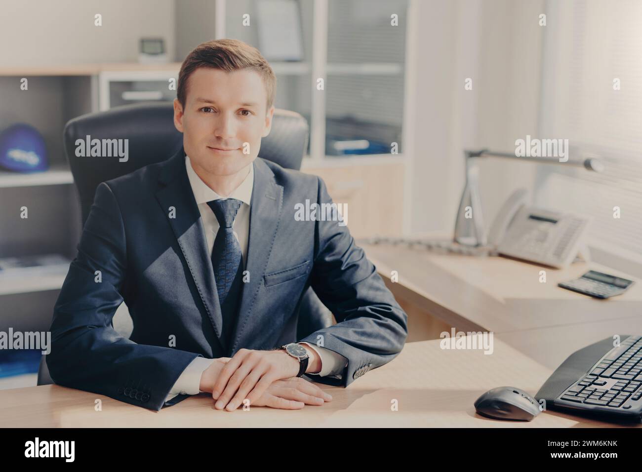 Confident businessman smiles gently in a well-lit office setting, exuding professionalism. Stock Photo
