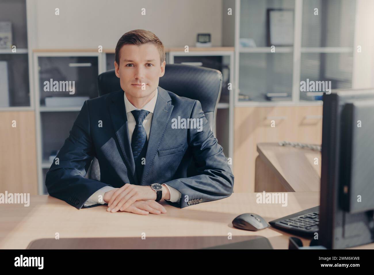Poised executive sitting assertively at his desk in a well-lit professional workspace. Stock Photo