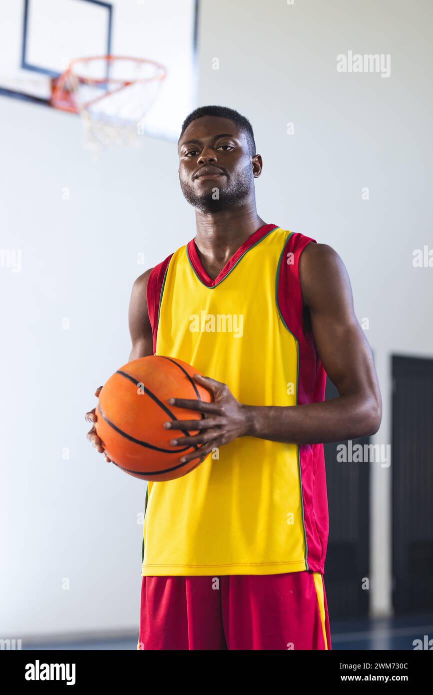 Confident African American man holds a basketball in a gym. His athletic stance conveys