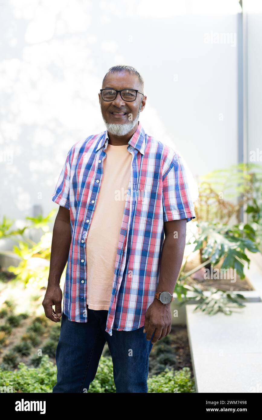 Senior biracial man stands smiling in a sunny garden at home Stock Photo