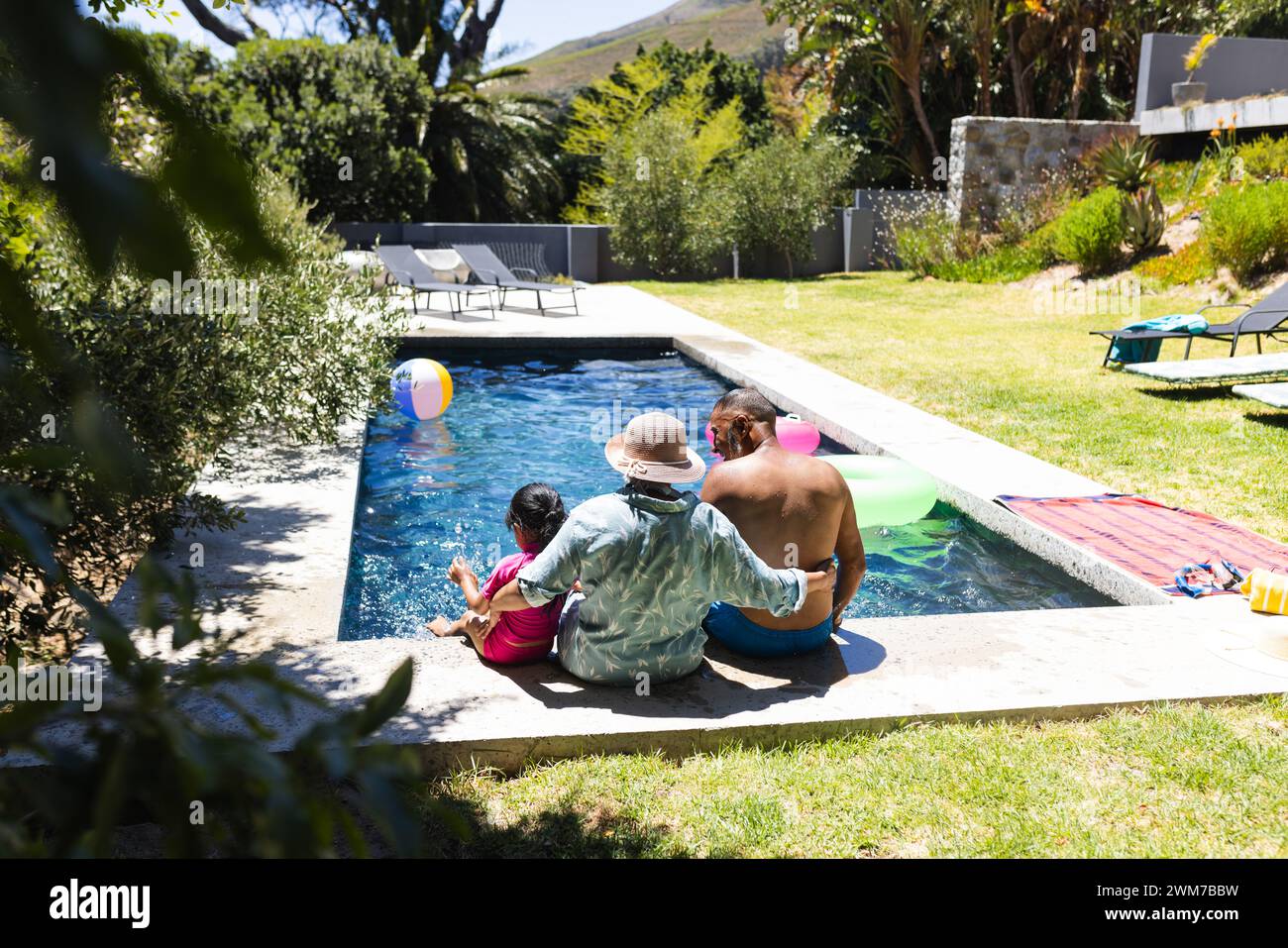 Biracial grandparents and granddaughter enjoy poolside fun at home with copy space Stock Photo