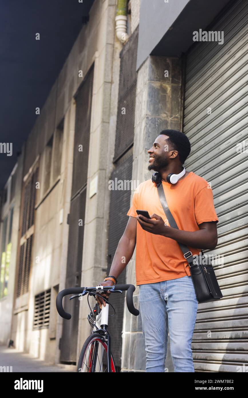 A young African American man stands by his bike outdoors in the city with copy space Stock Photo