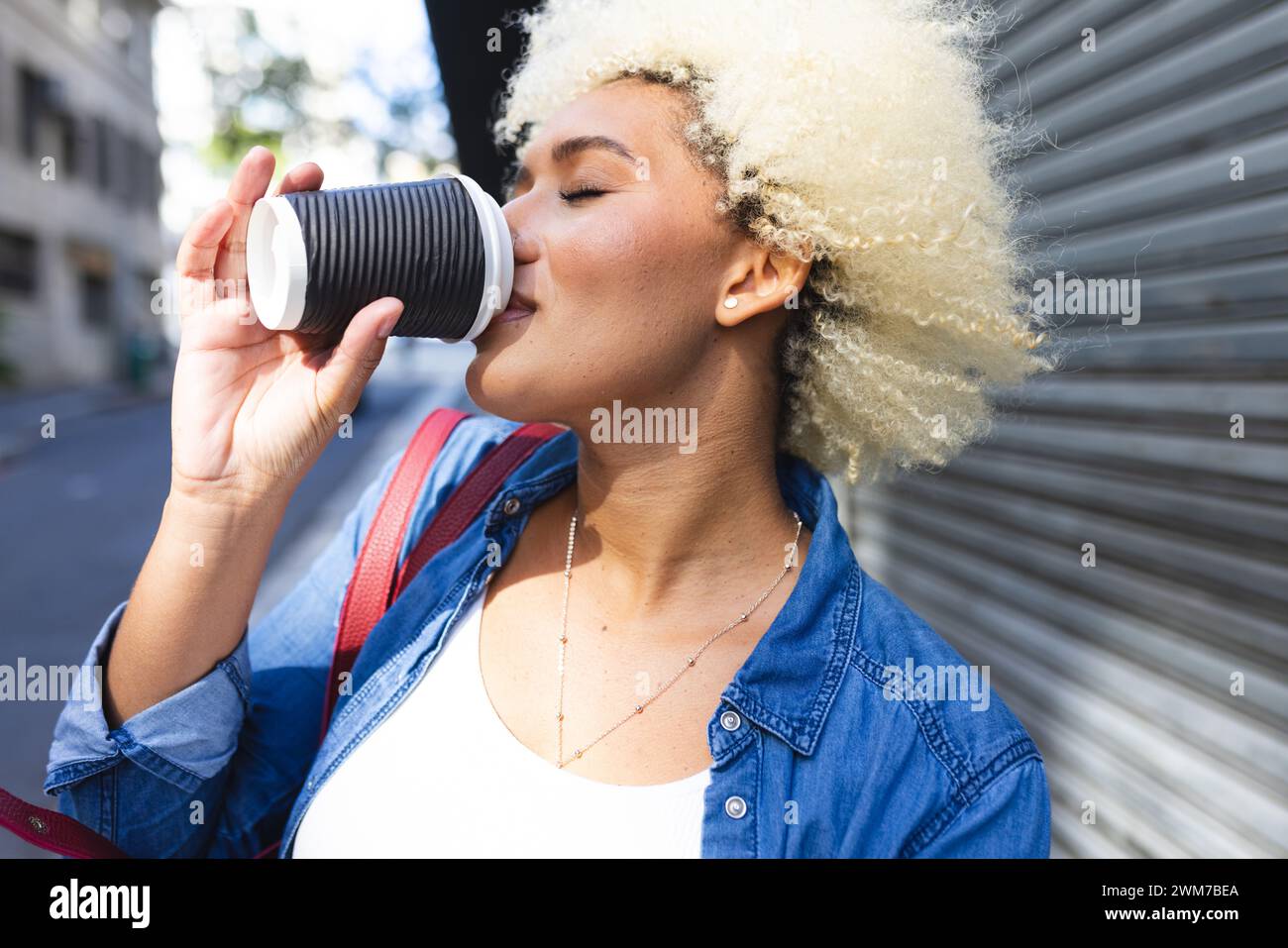 Young biracial woman enjoys a coffee outdoors in the city Stock Photo