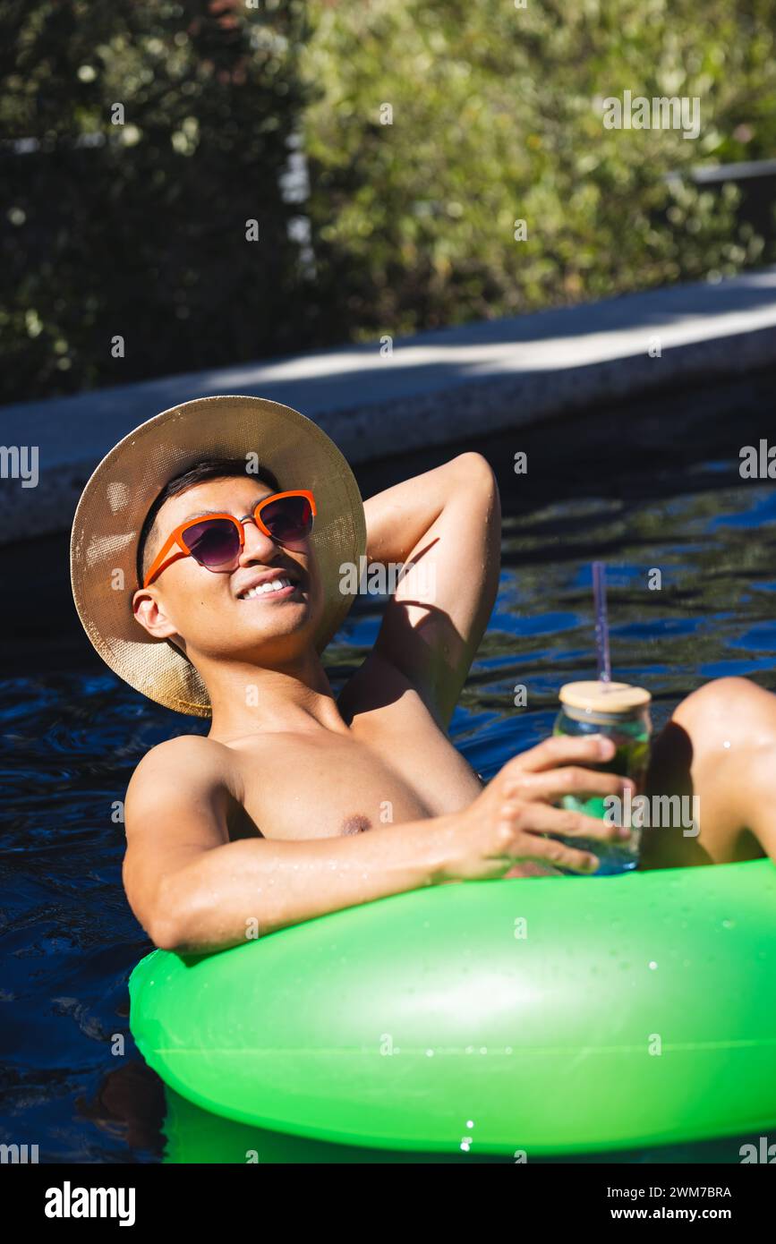 Young Asian man enjoys a sunny day floating in a pool, with copy space Stock Photo