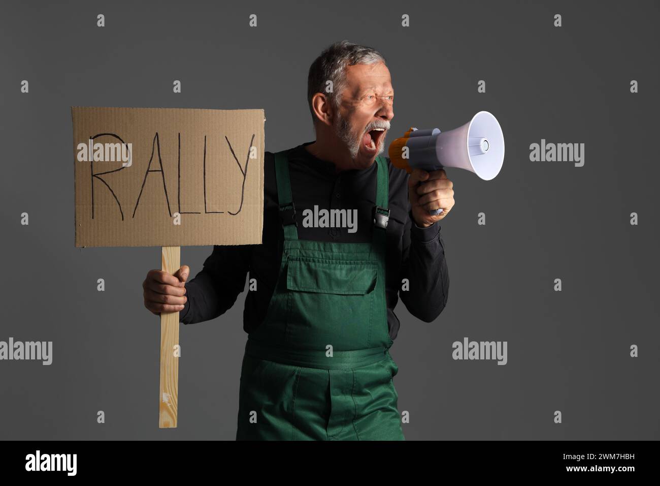 Protesting miner man with placard shouting into megaphone on dark background Stock Photo