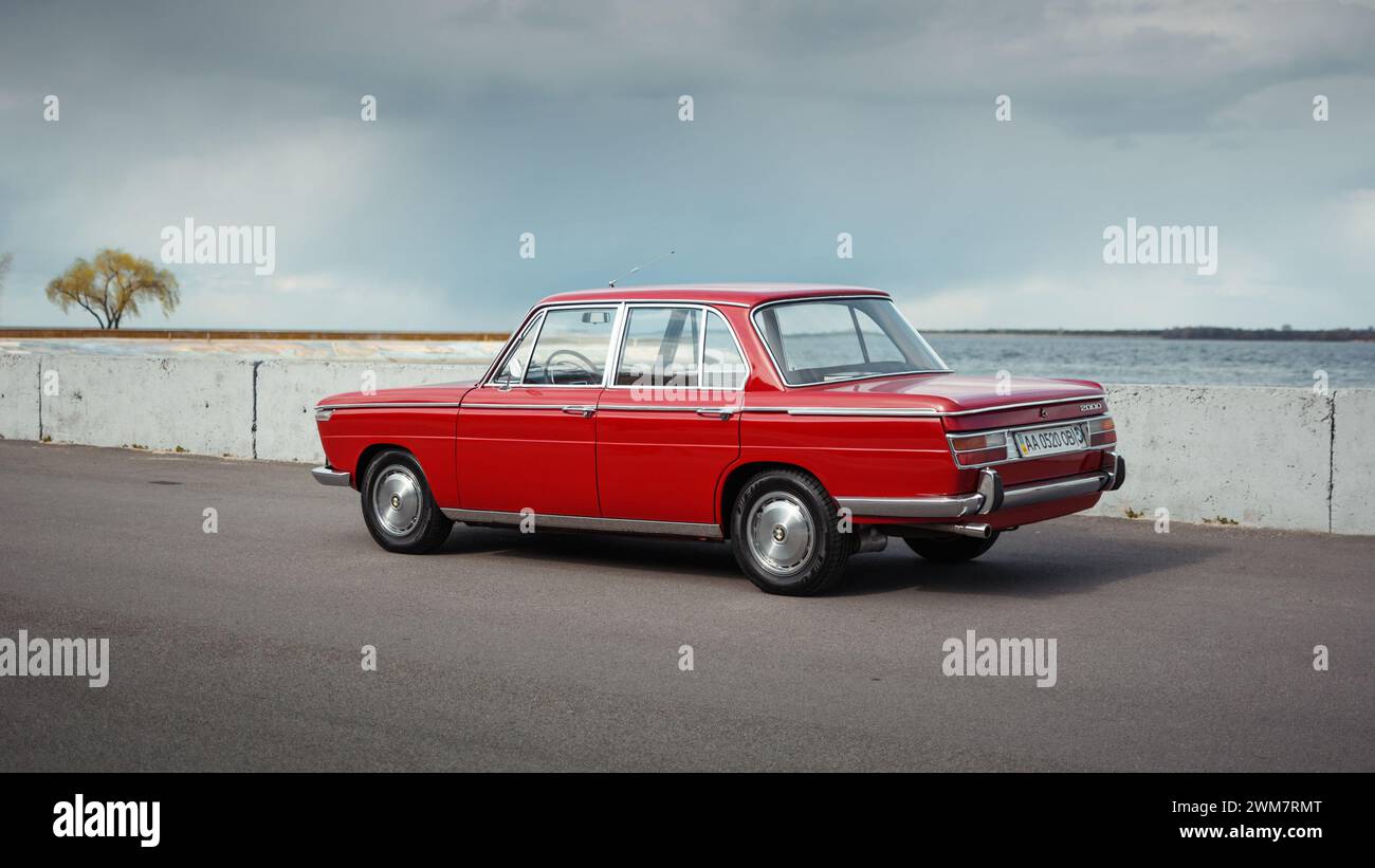 Red classic BMW from 1960s. Three quarter view of german sedan parked near concrete barrier and lake in the background Stock Photo