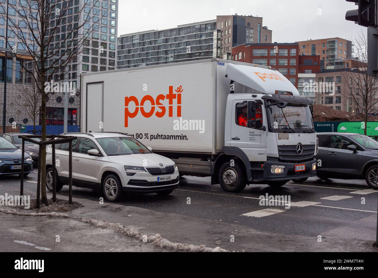 A Posti delivery truck is parked on a city street, with cars and urban buildings in the background; the image captures everyday urban life. Stock Photo