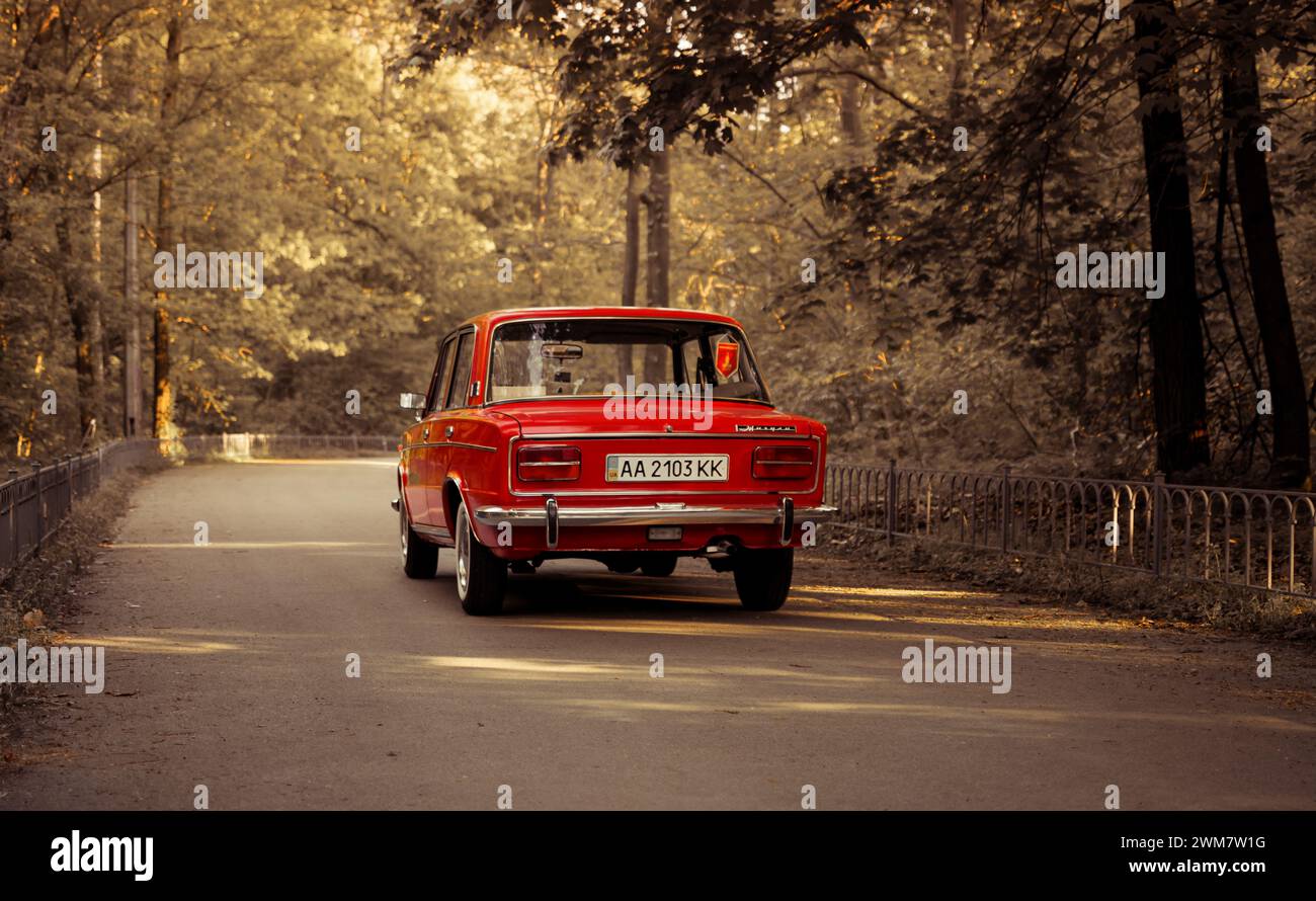 classic VAZ 2103 sedan from 1970s on forest road. Red Lada shot during golden hour - three quarter rear view. Stock Photo