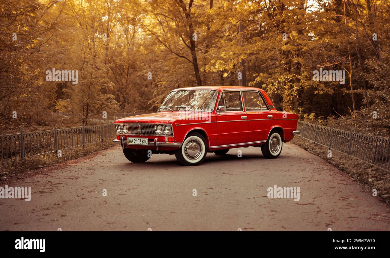 classic VAZ 2103 sedan from 1970s on forest road. Red Lada shot during golden hour - three quarter front view. Stock Photo