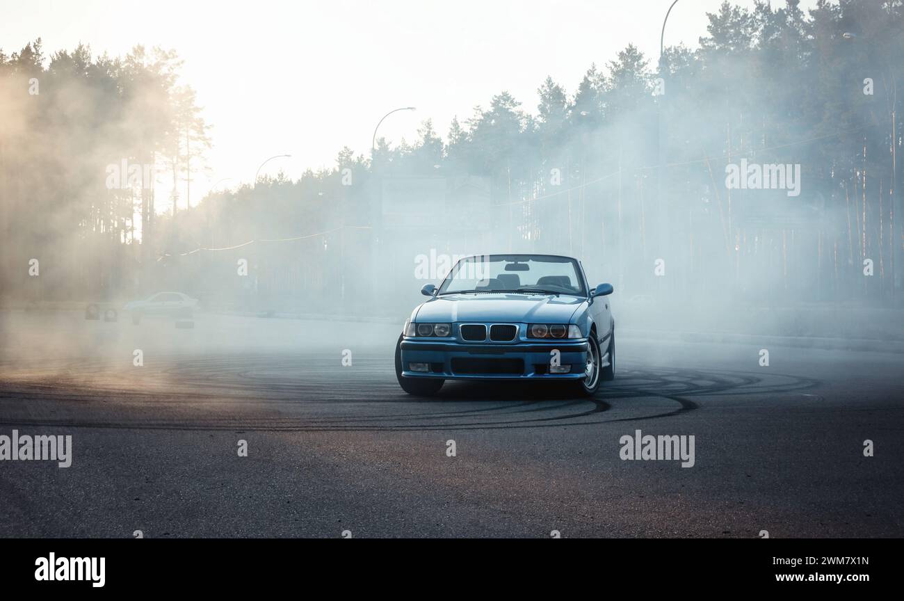 blue BMW M3 (E36 ) on a big parking lot covered with tire smoke. Front view of cabriolet on paved ground near the forest. Stock Photo