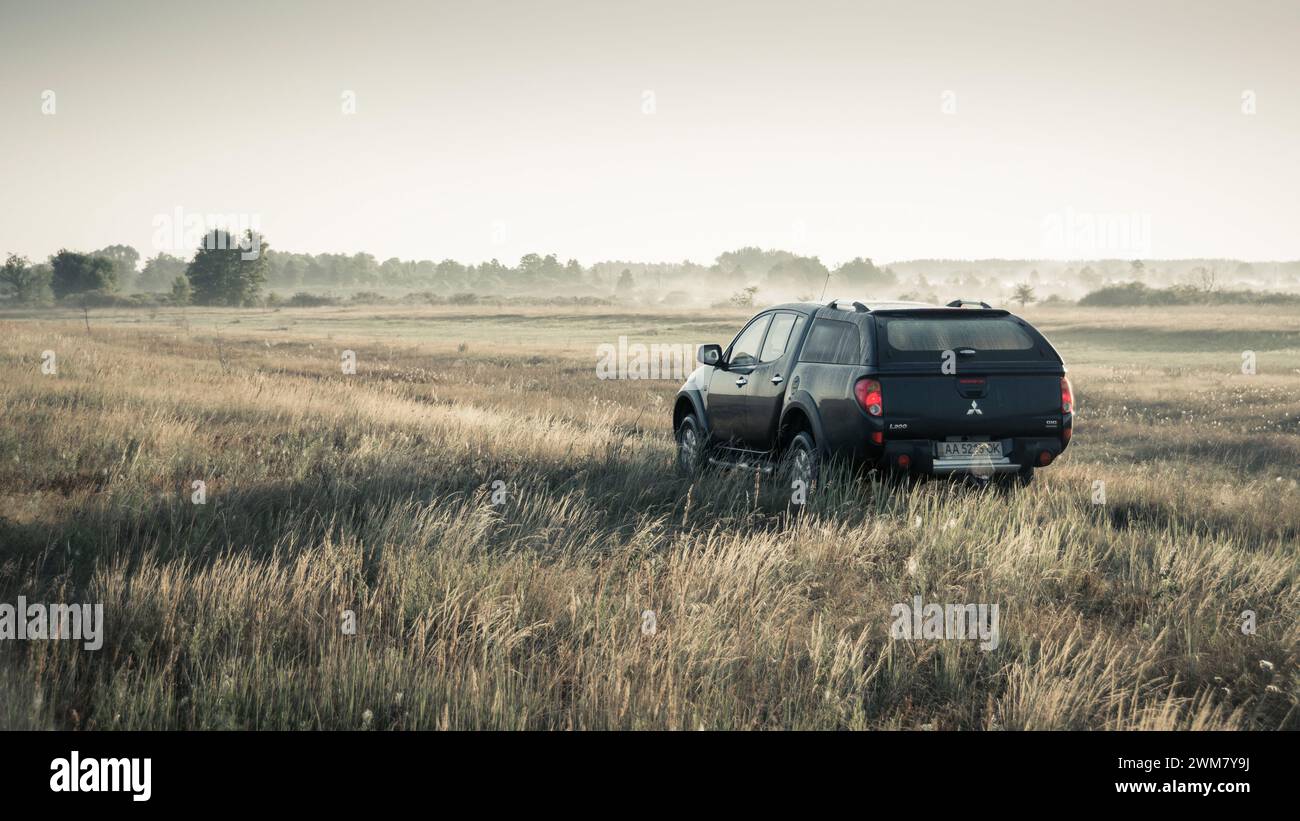 black Mitsubishi SUV pickup truck in a meadow. Morning light at 6am, rear three quarter view. Stock Photo