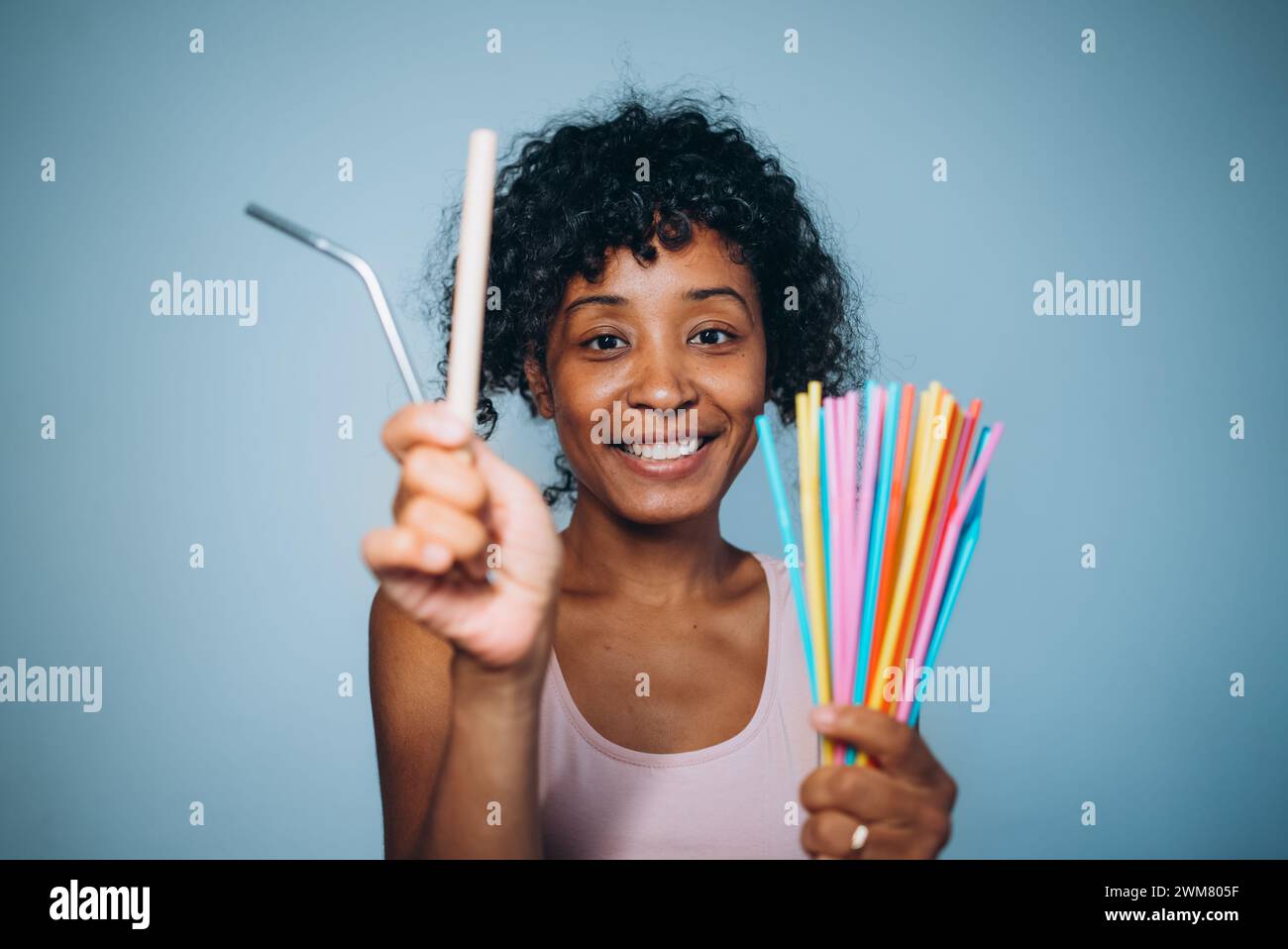 A cheerful woman presents a reusable metal straw and a bouquet of colorful plastic straws, advocating for eco-friendly choices. Reasonable consumption, concern for the environment. Stock Photo