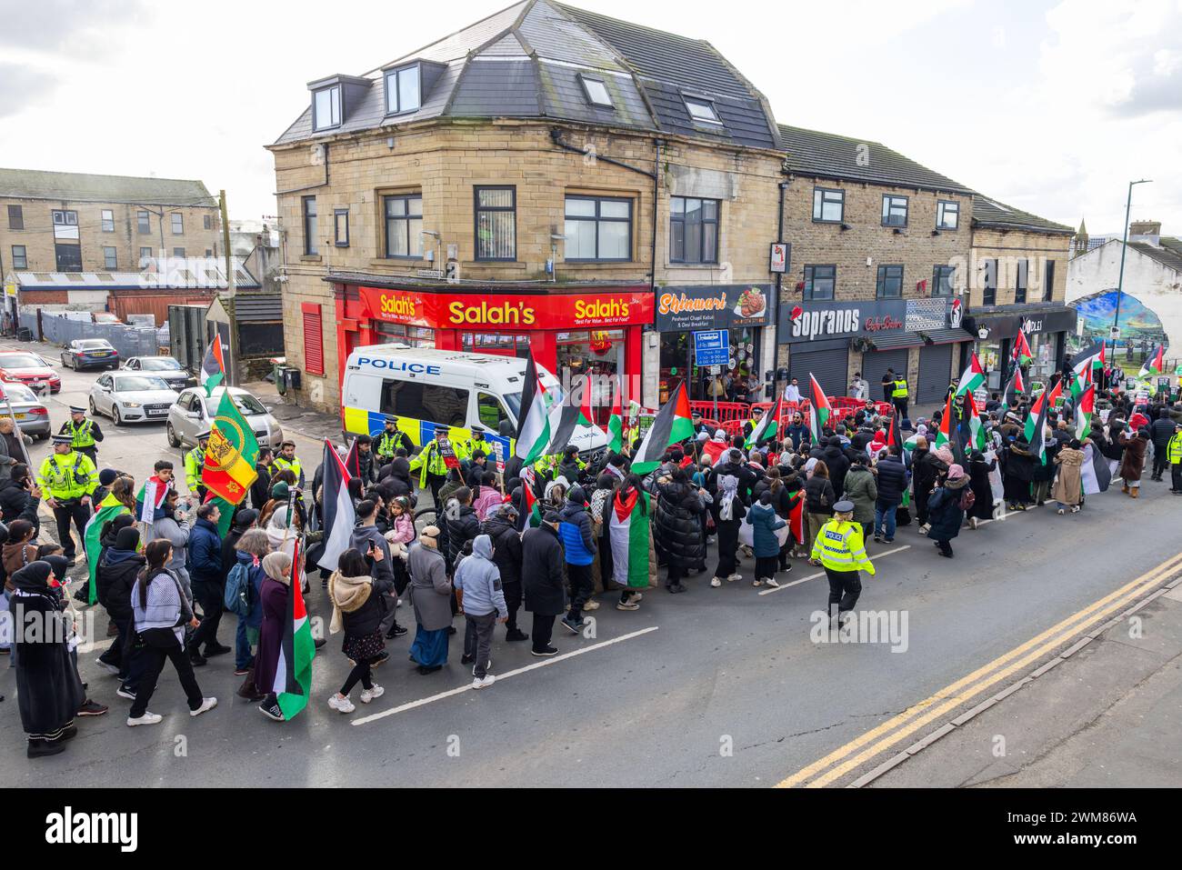 Bradford, UK. 24 FEB, 2024. Police protect Salah's takeaway on Leeds road as the West Yorkshire March for Palestine passes chanting towards the shop. The shop can still be seen to be damaged following a violent confrontation between shop owners and pro palestine protestors the night before following boycott dispute.  Credit Milo Chandler/Alamy Live News Stock Photo