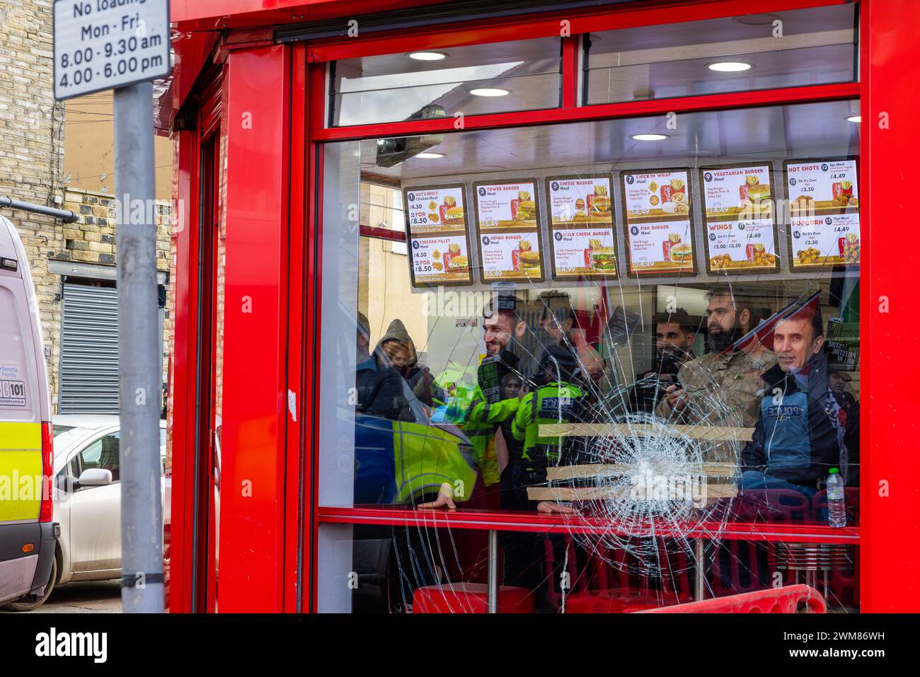 Bradford, UK. 24 FEB, 2024. Customers look out from Salah's takeaway on Leeds road as the West Yorkshire March for Palestine passes chanting towards the shop. The shop can still be seen to be damaged following a violent confrontation between shop owners and pro palestine protestors the night before following boycott dispute.  Credit Milo Chandler/Alamy Live News Stock Photo