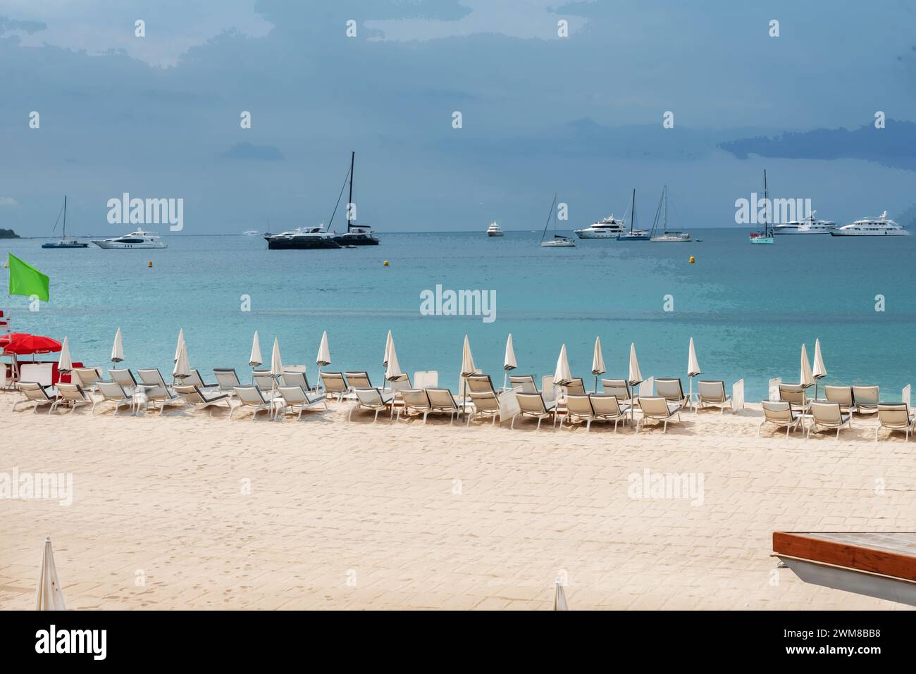 Fantastic relaxation view on small private sandy beach (with beach chairs and umbrellas) and Bay of Cannes: boats moving or anchored.  Maybe catamaran Stock Photo