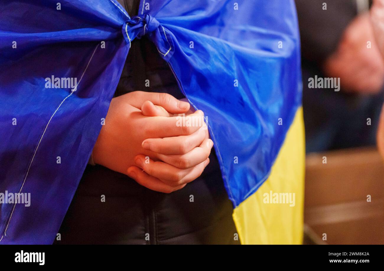 24 February 2024, Hesse, Frankfurt/Main: A man with a Ukrainian flag holds his hands folded in prayer. An ecumenical prayer for Ukraine was held in St. Bartholomew's Cathedral under the title 'Light will prevail over darkness'. Afterwards, people commemorated with candles in the cathedral square. Photo: Andreas Arnold/dpa Stock Photo