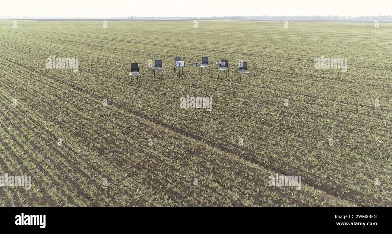 Six chairs in the middle of a empty winter crop field waiting for an orchestra musicians Stock Photo