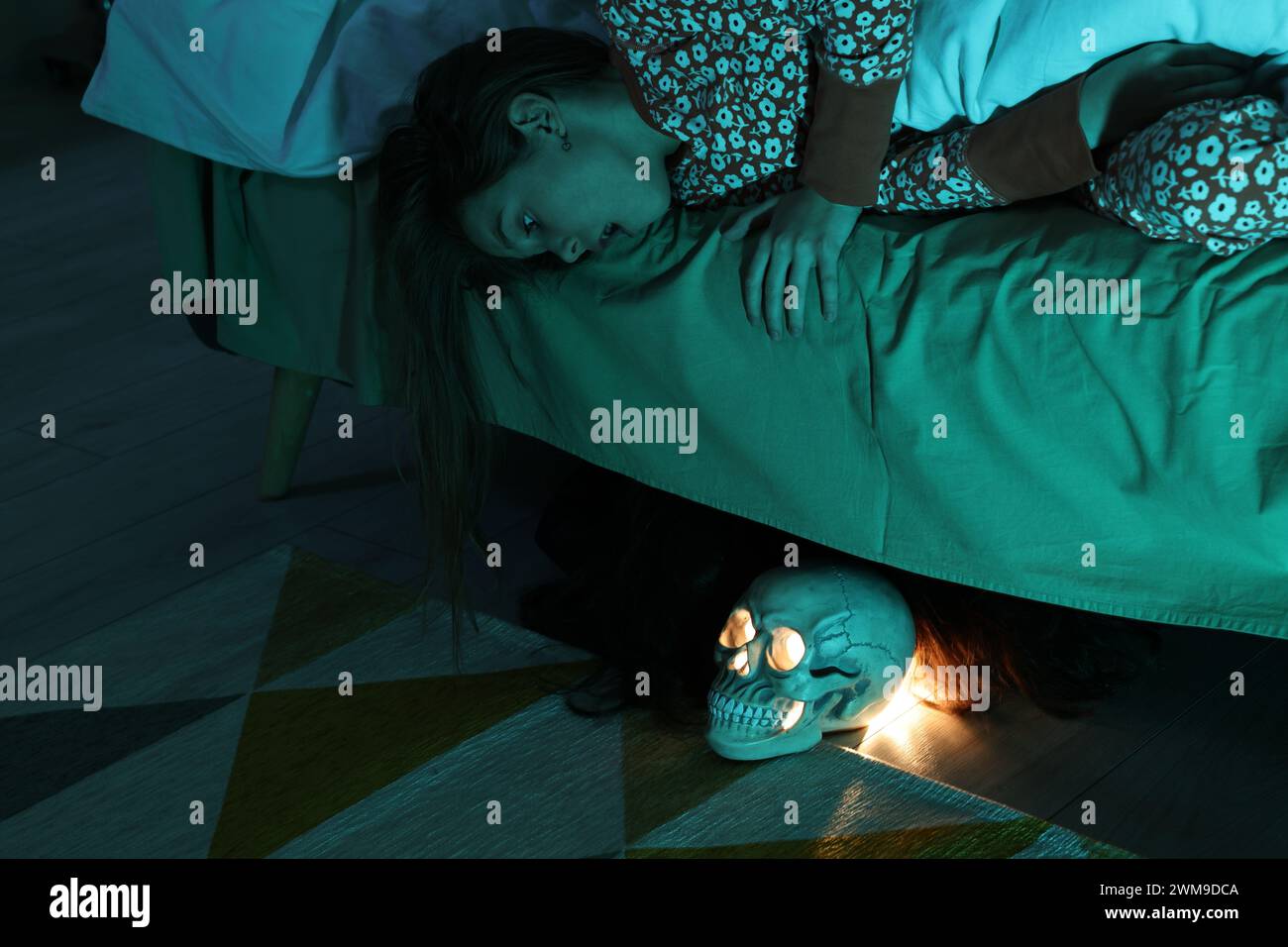 Childhood phobia. Scared girl looking at skull under bed indoors Stock