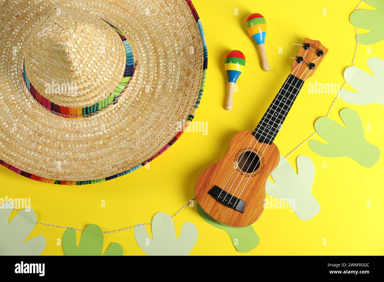 Mexican sombrero hat, maracas, ukulele and garland on yellow background