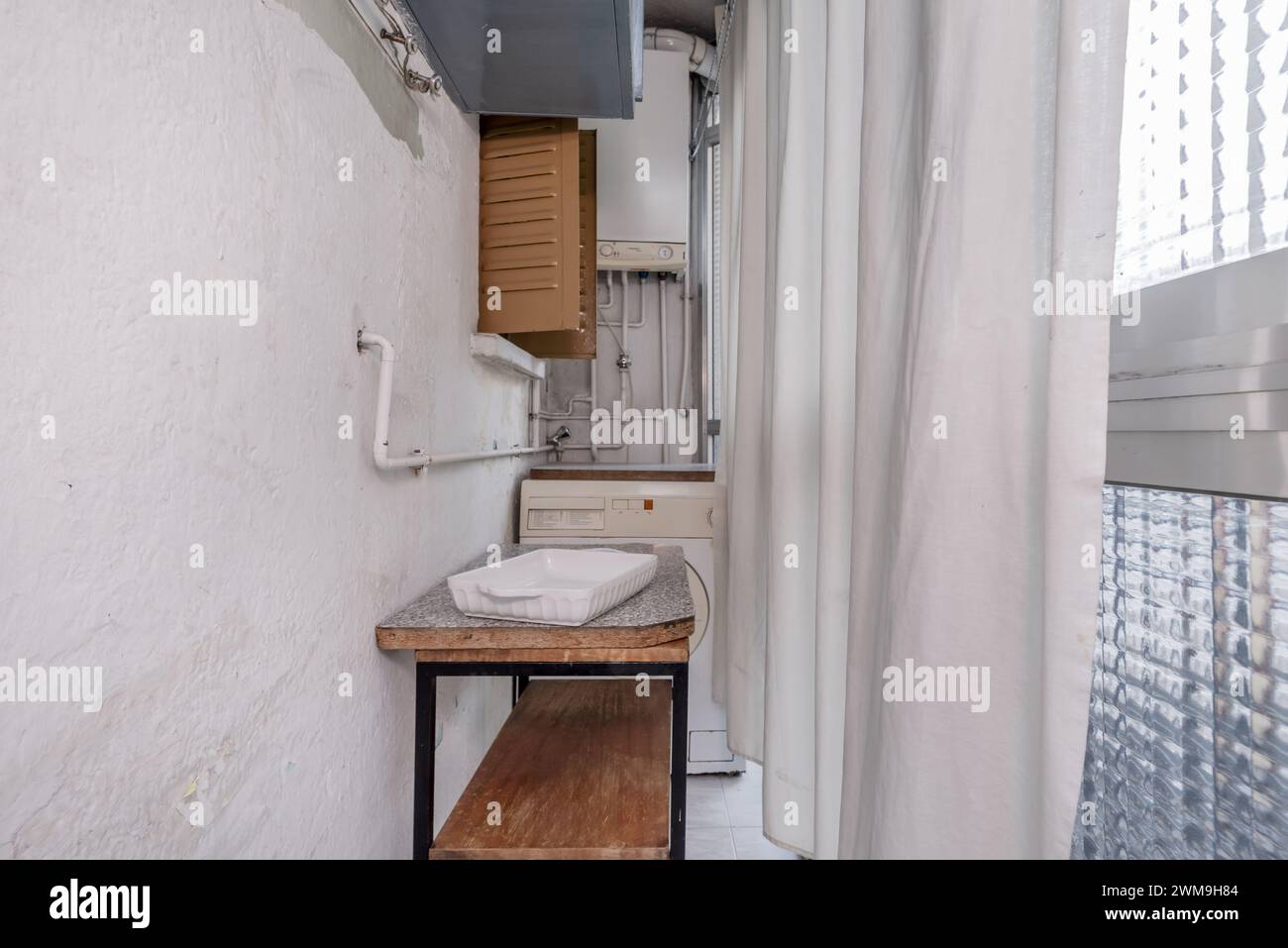 A small terrace balcony with metal windows and glass and aluminum doors, a washing machine and a water heater Stock Photo