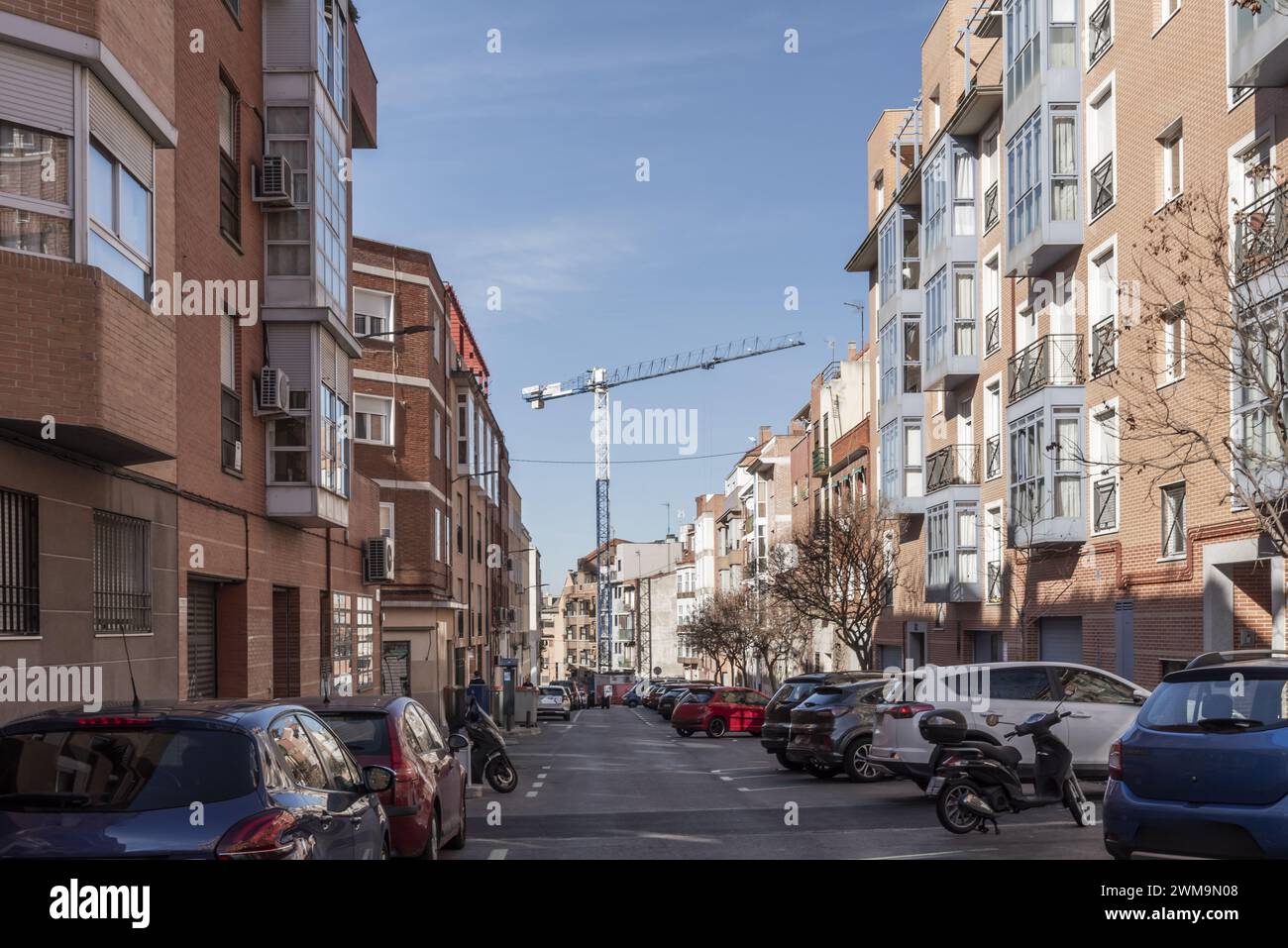 An urban street with modern low-rise buildings and battery-parked vehicles and a large construction crane in the background Stock Photo