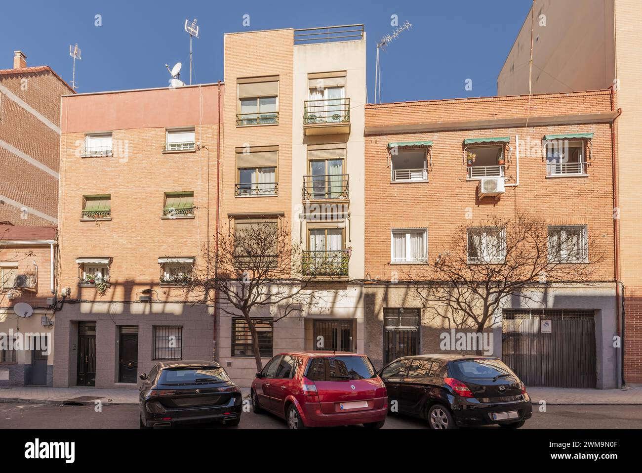 Facades of low-rise residential buildings on an urban street with vehicles parked in battery mode Stock Photo