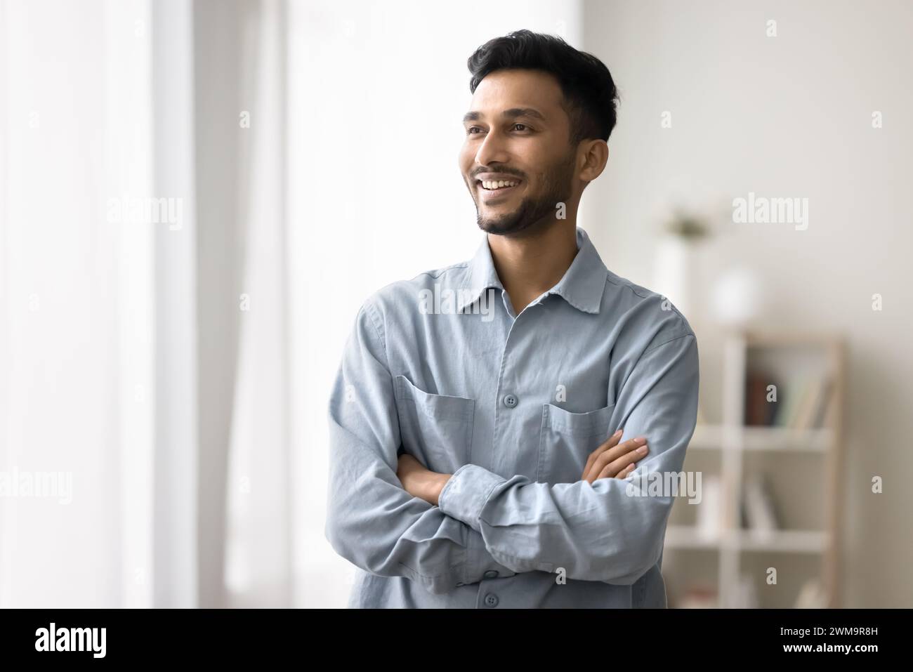 Indian man standing with arms crossed smiling looking away Stock Photo