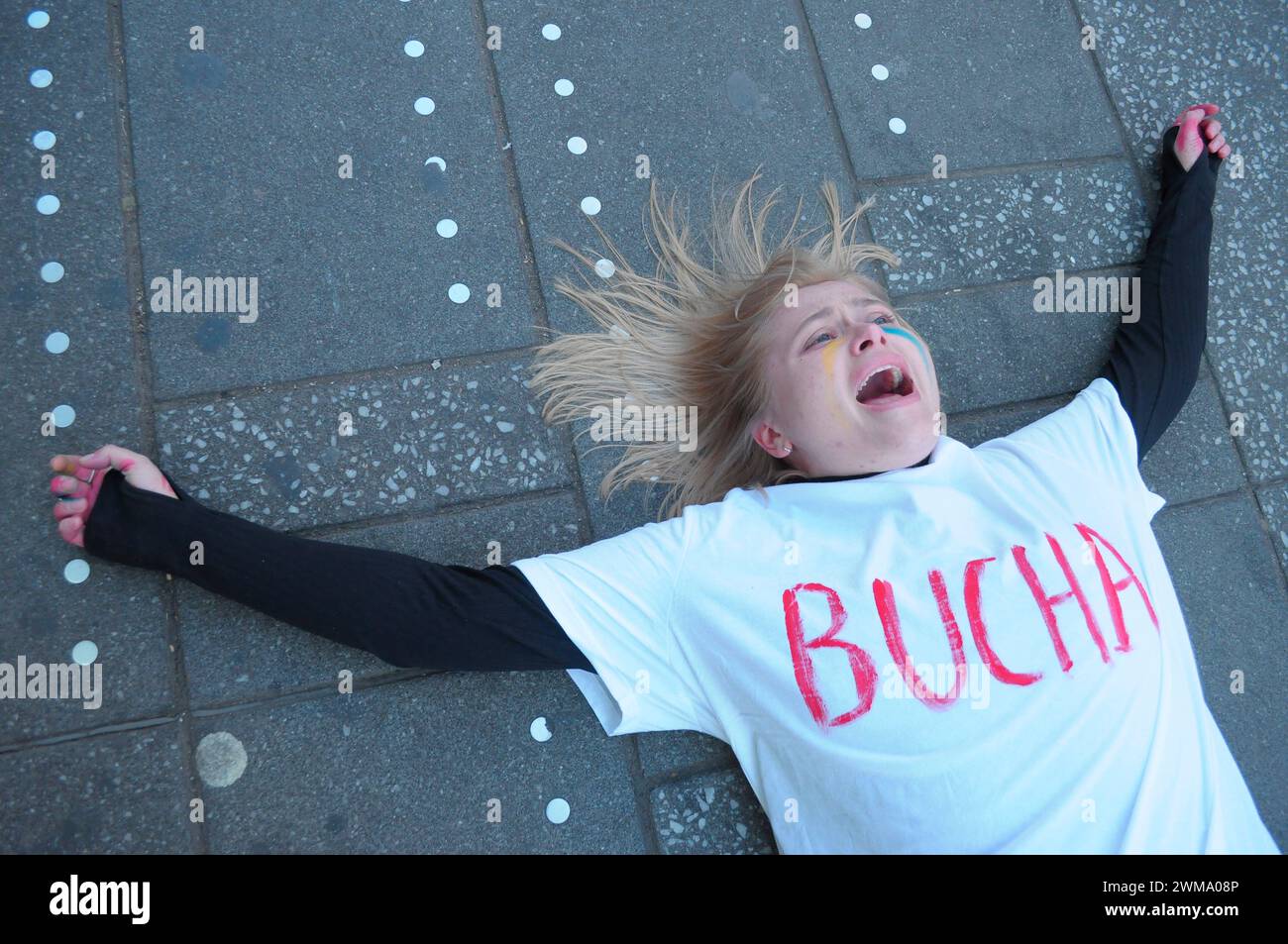 A pro-Ukraine demonstrator wearing a t-shirt with a name of a Ukrainian city written on it, performs a 'die-in' protest in Times Square. Demonstrators rallied in Manhattan, New York City on the two-year anniversary of the Russian invasion of Ukraine. Protestors condemned the invasion and opposed Russian President, Vladimir Putin. Last weekend, Russian forces captured the eastern Ukrainian city of Avdiivka located on the front line. The loss of the city comes as a $60 billion aid package for Ukraine from the United States has been stalled following disagreements in Congress. Ukrainian President Stock Photo