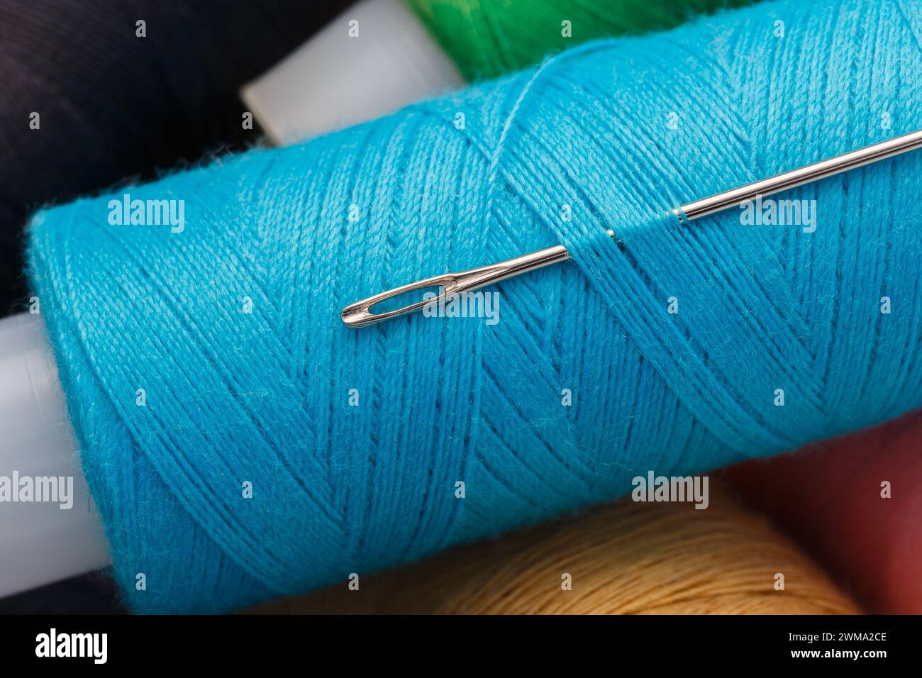 Multi-colored threads on spools and a steel needle. Macro photography, close-up Stock Photo