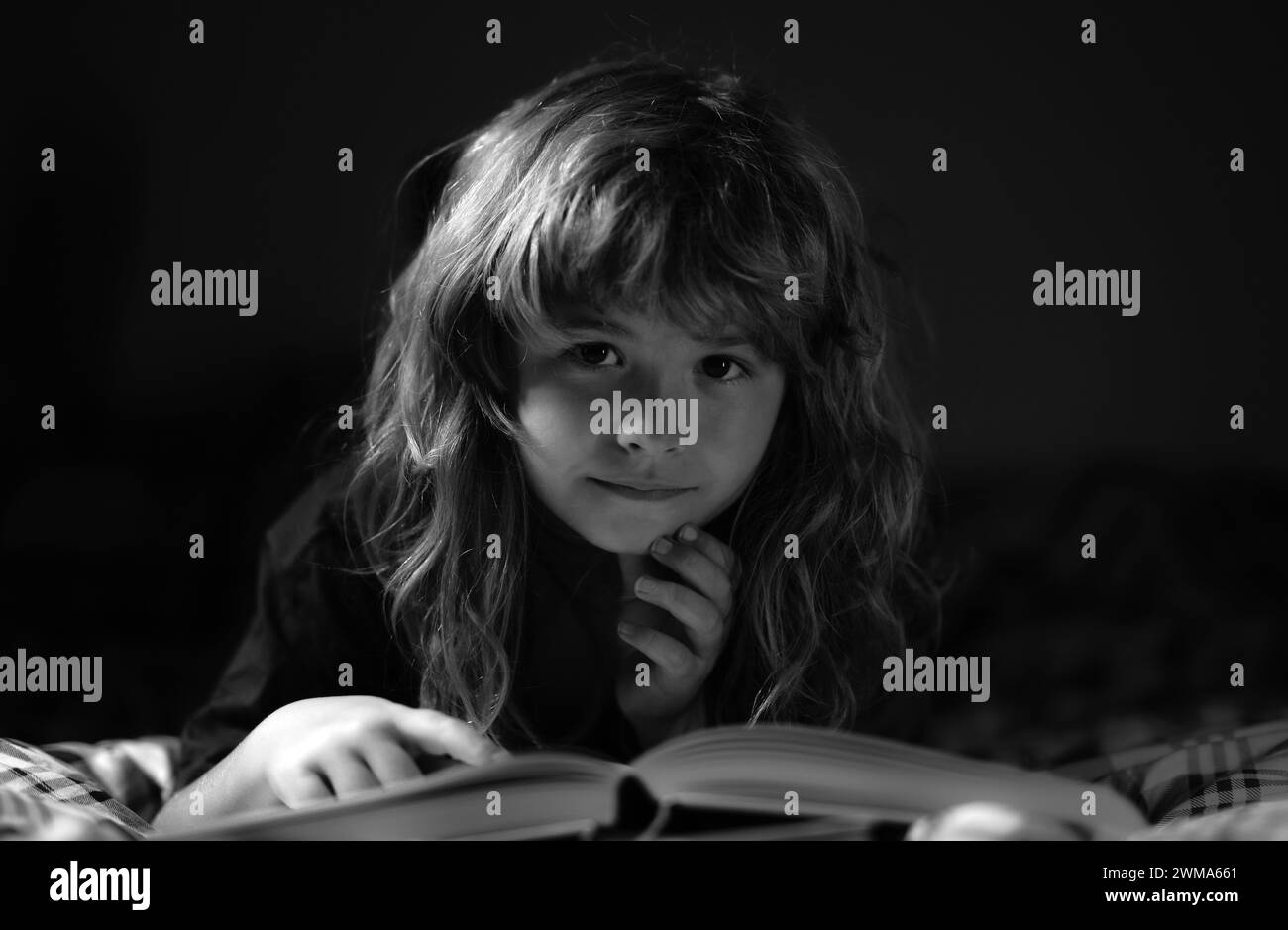 A little cute boy reading a book lying on the bed. Bedtime story, kids