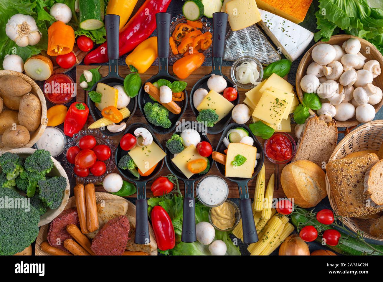 Filled raclette pans with a rich selection of cheese, vegetables and vegetarian meat substitutes, appetisingly presented Stock Photo