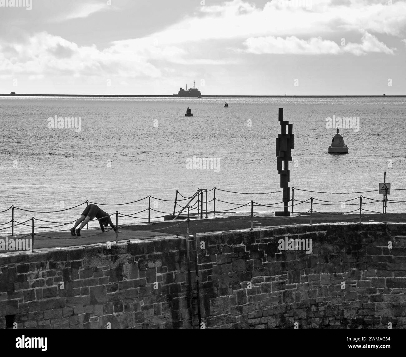 Press Up execises or worshiping fine art, a young man with Sir Anthony Gormley’s ‘Look II’ 12ft sculpture on West Hoe Pier Plymouth. The controversial Stock Photo