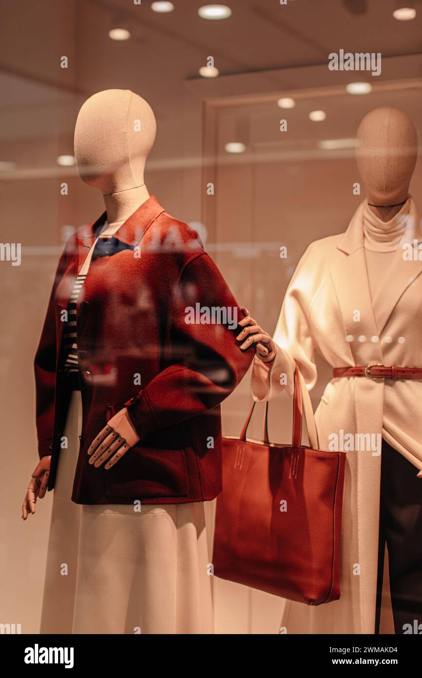Two stylish mannequins in a store window dressed in seasonal fashion cloth. Brown jacket, white long coat, brown leather bag Stock Photo
