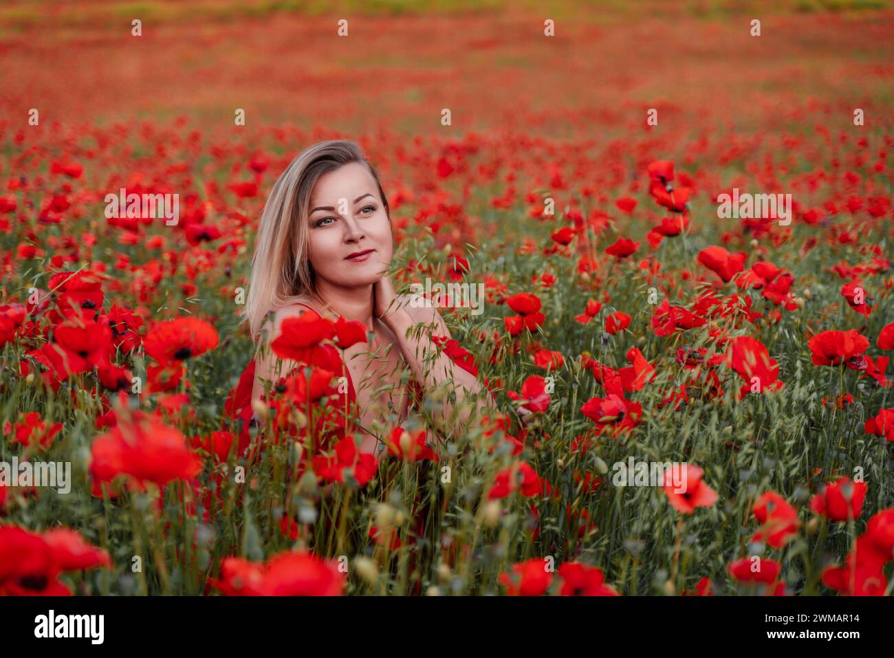 Happy woman in a red dress in a beautiful large poppy field. Blond sits ...