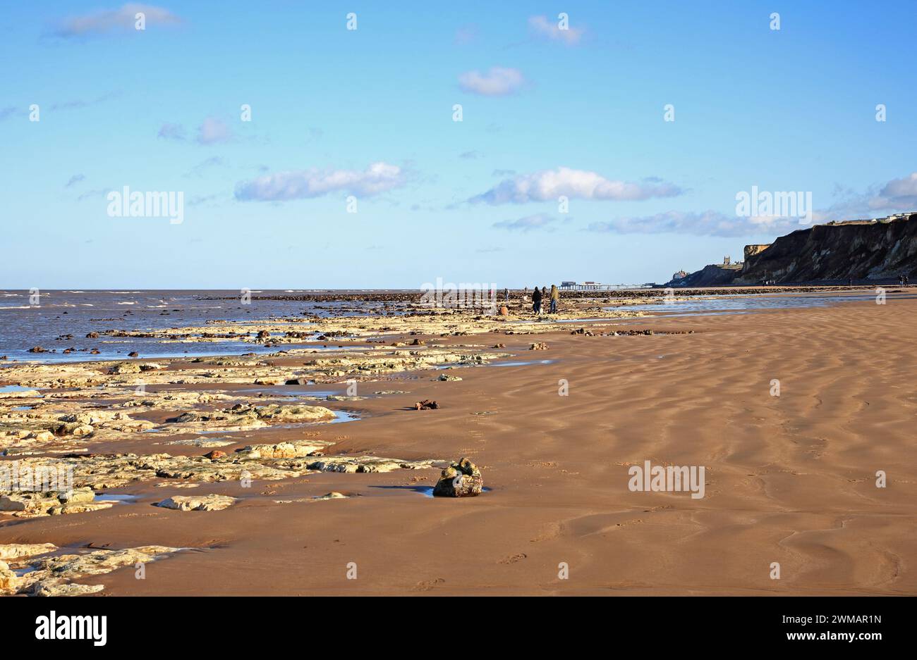 A view of the beach at low water during a spring tide with people walking the shoreline at West Runton, Norfolk, England, United Kingdom. Stock Photo