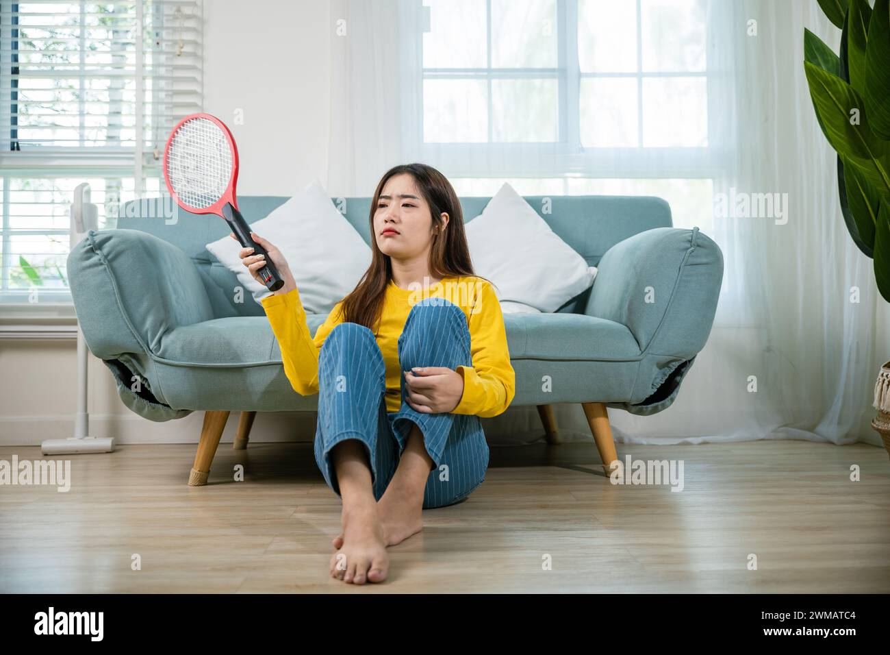 woman sitting floor using mosquito swatter or electric net racket Stock Photo