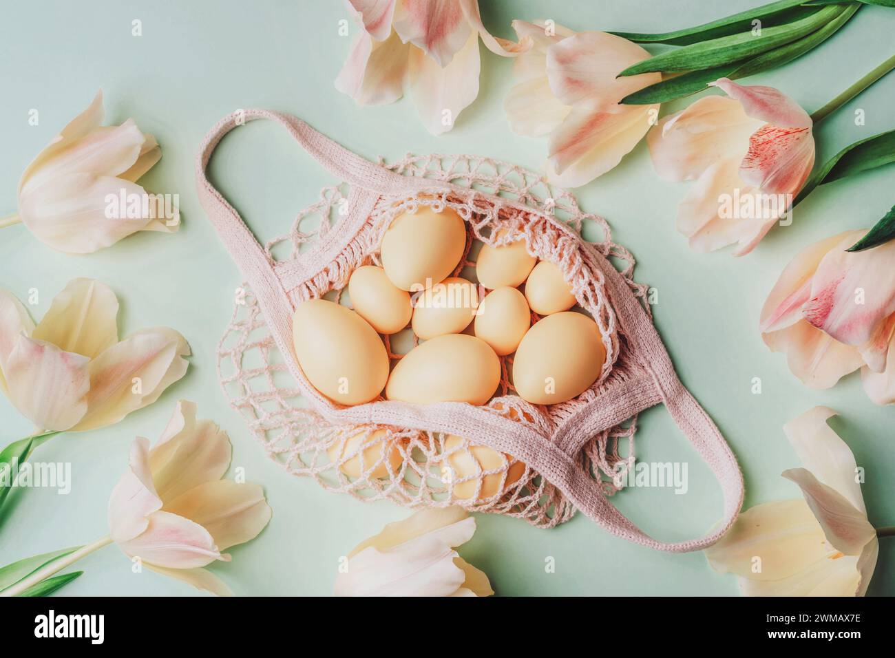 String bag with Easter eggs and yellow tulips on light green background. Top view, flat lay. Stock Photo