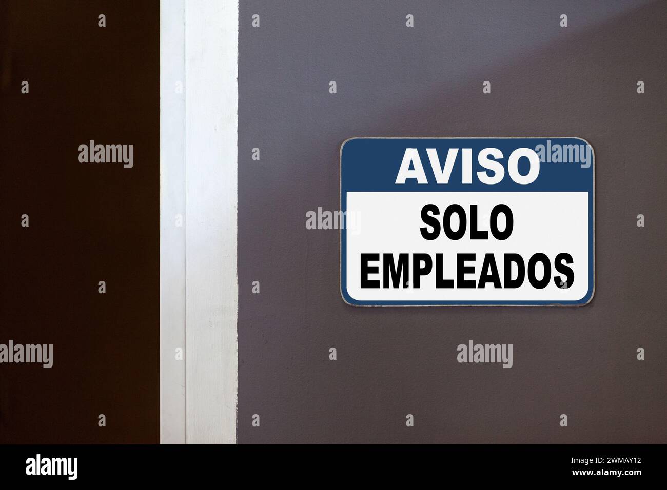 Blue and white notice sign on the side of an open door stating in Spanish : 'Aviso, Solo empleados', meaning 'Notice, Employees only'. Stock Photo